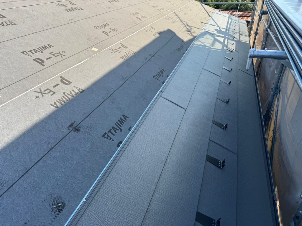 スーパーガルテクト屋根材(シェイドチャコール)を板金として貼り付けている様子。高品質で耐久性の高い屋根リフォーム工程