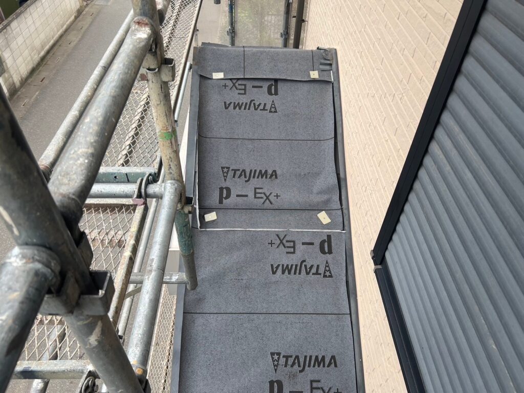 下屋根カバー工法で防水シートを丁寧に貼り付けている写真。雨漏り防止の要となる高耐久の防水工程。